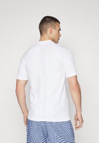 Camisa blanca de manga corta con textura suave y corte ajustado. Presenta un diseño de patrón sutil en la parte trasera y un cuello acanalado.
