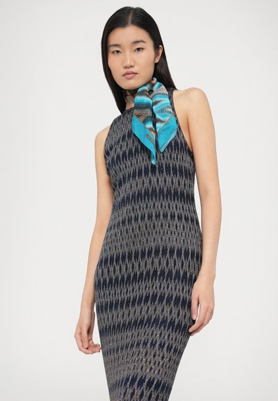 Megzta rankovių suknelė su geometriniu raštu mėlynos ir pilkos spalvų, papildyta turkio spalvos šilko skara, surišta prie kaklo.