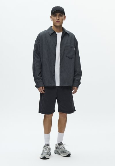 Sort-hvidstribet oversized skjorte med knapper, hvid t-shirt, sorte shorts, hvide sokker og grå sneakers. Enkel design og afslappet pasform.