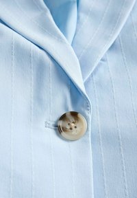 Ύφασμα σακακιού ανοιχτού μπλε με λεπτές ρίγες και μαρμάρινο μπεζ κουμπί με τέσσερις τρύπες, στερεωμένο κοντά στον γιακά.