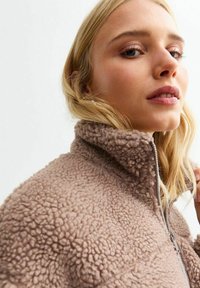 Fleece jas in lichtbruin met een hoge kraag en rits. Gelaagd fabric met een zachte, pluizige uitstraling. Minimalistisch ontwerp.