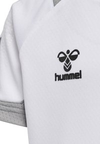 Vit atletisk t-shirt tillverkad av texturerat tyg med grå accenter. Har en svart tryckt logotyp "hummel" och en distinkt design detalj på axeln.