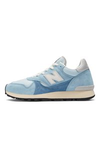 Hellblaue Sneakers aus Wildleder und Mesh-Materialien, mit einem weißen "N"-Logo, cremefarbenen Schnürsenkeln, einem grauen Fersenakzent und schwarzer Gummisohle.