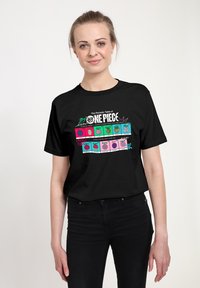 T-shirt en coton noir présentant un graphisme coloré du "Tableau périodique de One Piece" avec divers fruits et motifs textuels.