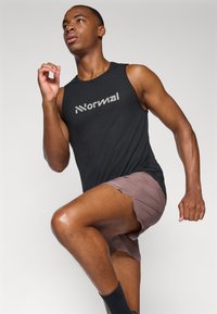 Sort ærmeløs atletisk skjorte med tekstureret stof og "Normal" logo, matchet med lysebrune løbeshorts og sorte sokker, i en dynamisk position.