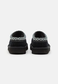Svarta tofflor med en mjuk textur, rund form och dekorerad med broderad kant i grönt och vitt runt kragen.
