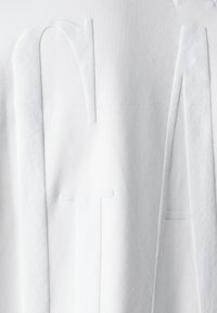 Acercamiento a una tela blanca con grandes letras en relieve y texturizadas "C", "T" y "A" grabadas en la superficie.