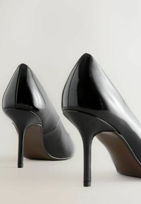 Fekete patent bőr magassarkú cipők hegyes orrformával és vékony stiletto sarokkal. Simított felület, minimális varrási részletek.