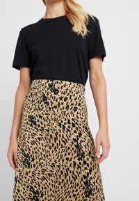 T-shirt nera abbinata a una gonna al ginocchio con un motivo leopardato in nero su sfondo beige, realizzata in tessuto leggero.