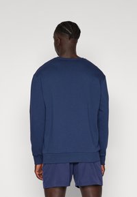 Sudadera azul marino con cuello redondo, mangas largas y dobladillo acanalado. Tejido de mezcla de algodón con una textura suave. Llevada sobre unos pantalones cortos a juego.