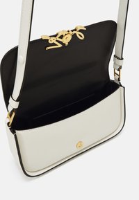 Sac en cuir blanc avec une doublure noire, doté d'une fermeture en métal doré et d'une texture lisse. Bords arrondis et accents notables.