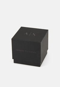 Scatola quadrata nera con finitura opaca, caratterizzata da un logo "A/X" in rilievo e dal testo "ARMANI EXCHANGE" in un colore contrastante sulla parte anteriore.