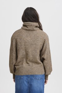 Brun stickad tröja med hög krage och sänkta axlar, texturerad tyg och ribbade fållar, i kombination med en jeanstam.