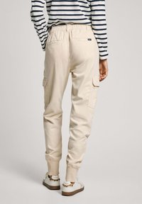 Beige cargo pants with an elastic waistband, side pockets, and cuffed hems. Worn with a navy and white striped top and casual sneakers.