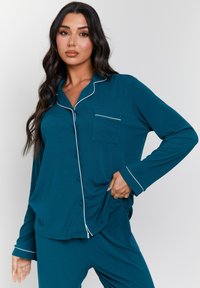 Teal pajama set in soft fabric featuring button-down shirt with collar, chest pocket, and white piping along cuffs and collar.
