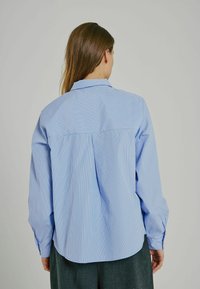 Blå och vit randig knapp-up skjorta, långärmad, med baksydda och rundad nederkant. Materialet verkar lättviktigt och har en slät textur.