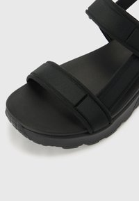 Black sandal featuring two wide textile straps and a cushioned footbed. Thick rubber sole with textured patterns for grip.