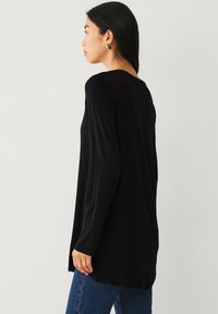 Haut noir à manches longues avec une coupe décontractée, doté d'un ourlet arrondi et d'une texture lisse, associé à un jean en denim bleu.