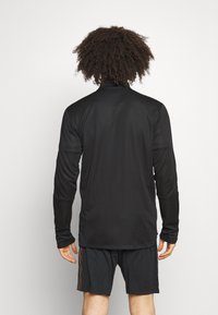 Langærmet, sort atletisk skjorte med høj krave og tommelhuller, lavet af glat, strækbart stof, parret med sorte shorts med sidelæns striber.