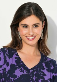 Violetti kukkapaidassa on V-pääntie, jossa on laivastonsiniset kukkakuviot. Kimaltavat hopeiset korvakorut modernilla muotoilulla täydentävät ilmeen.