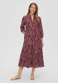 Bordeaux lange mouw jurk met abstract wit geometrisch patroon, tailleband, gelaagde rok en zijzakken. G gedragen met platte sandalen.
