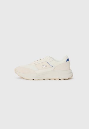 Off-white low-top sneaker with lace-up design, beige suede accents, blue heel tab, and brand logo on the side.