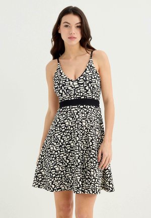 Vestido negro y crema con escote en V y patrón geométrico abstracto, con cuerpo ajustado y falda acampanada. Presenta tirantes finos y una cintura negra.