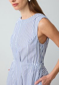 Blau-weißen gestreiften Kleid mit Rundhalsausschnitt, ärmellosem Design, gerafftem Taillenbereich und seitlichen Taschen. Glatte Stofftextur.