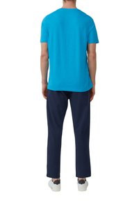 Türkises Baumwoll-T-Shirt mit kurzen Ärmeln, kombiniert mit navyblauen Hosen. Model trägt weiße Sneakers mit dunklen Akzenten.