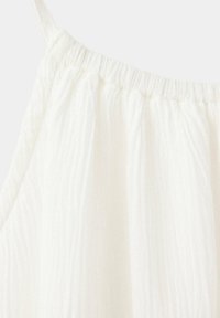 Vêtement blanc sans manches en tissu léger et texturé avec un col élastique froncé et une fine bretelle d'épaule.