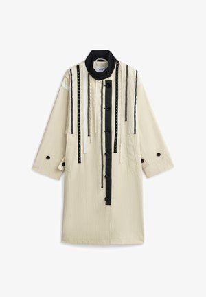 Lungo cappotto crema con colletto alto nero, strisce verticali nere, nastri decorativi e chiusura frontale con bottoni.