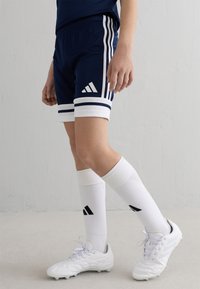 Navyshorts med vita ränder och en Adidas-logga, parat med vita strumpor med svarta accenter och vita träningsskor med texturerad yta.