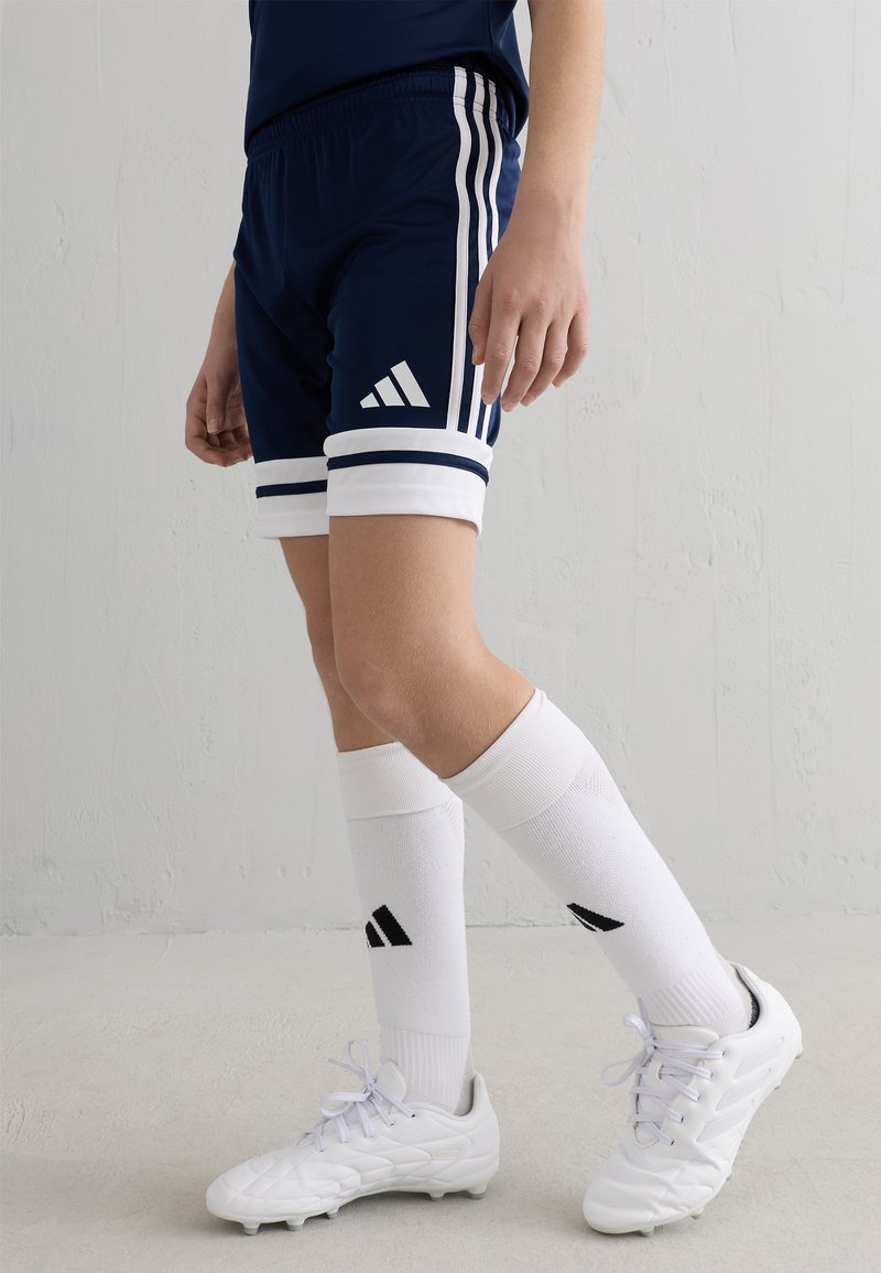 Navyshorts med vita ränder och en Adidas-logga, parat med vita strumpor med svarta accenter och vita träningsskor med texturerad yta.