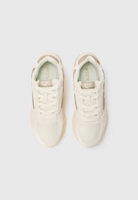 Baskets de sport blanches avec des accents beiges, tige en mesh et textile, bout rond, fermeture à lacets et semelle en caoutchouc pour une meilleure traction.