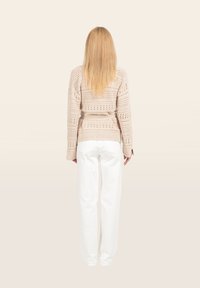 Beigefarbener Strickpullover mit Lochmuster, ausgestattet mit einem gebundenen Gürtel und langen Ärmeln, kombiniert mit weißen geraden Hosen.