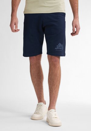 Marineblauwe shorts van zacht materiaal, met een subtiele logo-print op het linkerdij en een relaxed fit, gecombineerd met witte sneakers.
