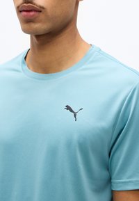 Νεαρός άνδρας που φορεί ανοιχτό μπλε μπλουζάκι Puma, εμφανίζοντας τον άνω κορμό και το λογότυπο Puma στο στήθος.