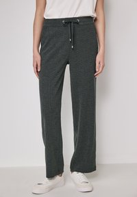 Mörkgrön, ribbad tyg, vida byxor med elastiskt midjeband och dragsko. Kombination med vita sneakers för en avslappnad look.