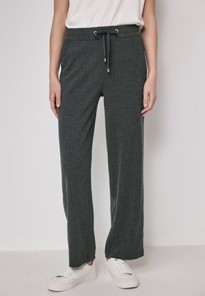 Donkergroene, geribbelde stof, wijde broek met een elastische tailleband en koord. Gecombineerd met witte sneakers voor een casual look.
