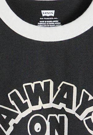 Schwarzes Levi's T-Shirt mit weißem Kragen und großem weißen Umrisstext "ALWAYS ON" auf der Vorderseite, Etikett zeigt Herstellung in Bangladesch an.