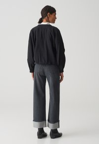Zwarte lichte blouse met pofmouwen, gecombineerd met donkergrijze wijde jeans met opgerolde manchetten en zwarte enkellaarzen.