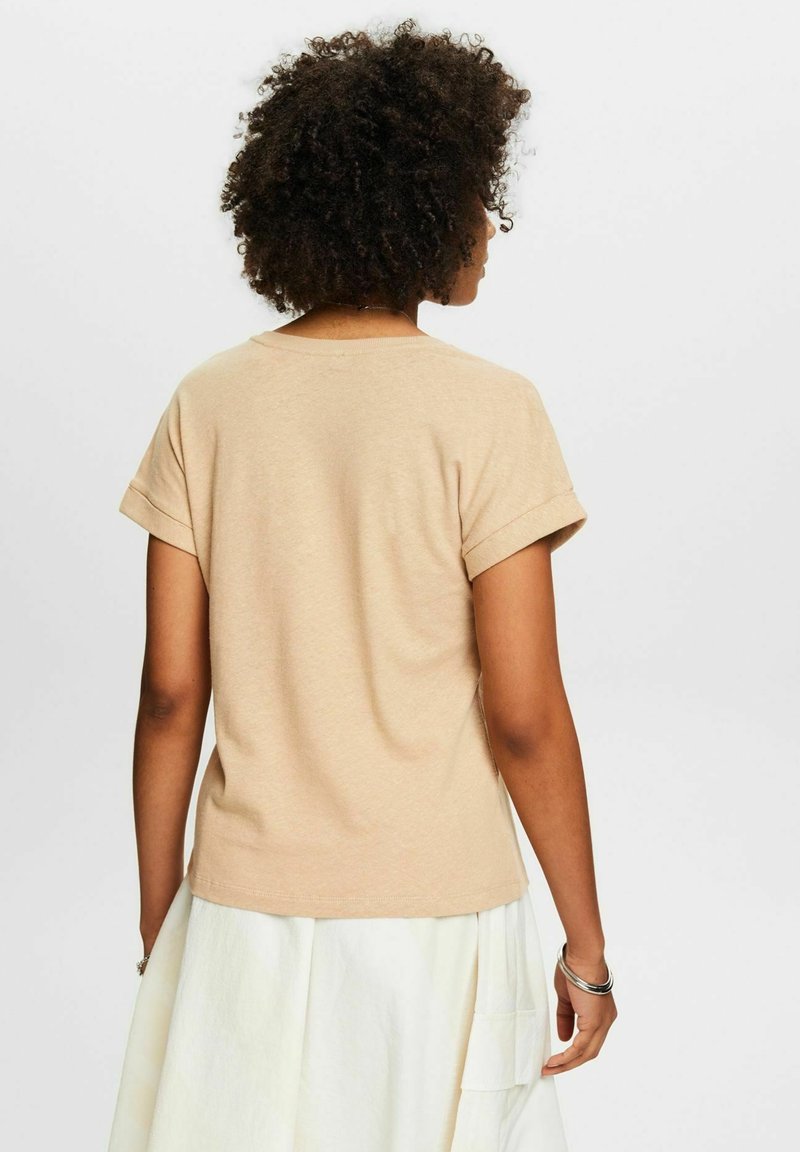 Beige Baumwoll-T-Shirt mit einem Rundhalsausschnitt und umgeschlagenen kurzen Ärmeln, das eine glatte Textur und eine lockere Passform an der Rückseite aufweist.