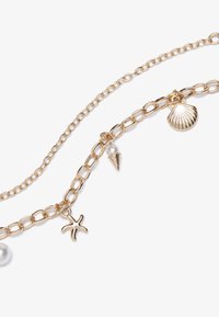 Gouden ketting met meerdere bedels: een schelp, een sterrenvis, een ijsje en een parel. Smooth textuur met een glanzende metalen afwerking.