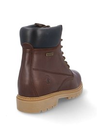 Botín de cuero marrón impermeable hasta el tobillo con cuello acolchado negro y suela beige con tacos, visto desde la parte trasera y lateral.