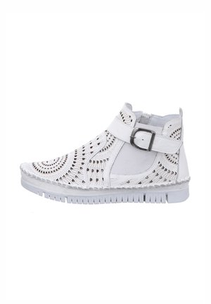 White ankle boot with cut-out detailing, textured surface, adjustable buckle strap, and a thick white rubber sole.