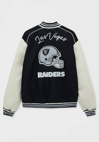 Zwarte en crèmekleurige jas met een ribgebreide kraag, voorzien van de tekst "Las Vegas" en "RAIDERS" en een zilveren helmlogo geborduurd op de achterkant.