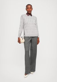 Gray cable-knit sweater with a maroon collar, paired with gray textured wide-leg trousers and a cream clutch bag. White pointed-toe shoes.