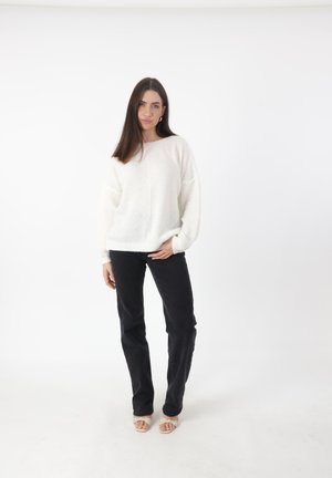 Witte gebreide trui met een gestructureerd patroon, verlaagde schouders, ontspannen pasvorm, gecombineerd met zwarte recht-toelopende broek en lichte open hakken.