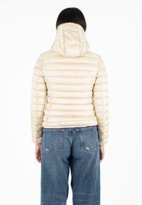 Lichtbeige pufferjack met horizontaal gestikte ontwerp, vaste capuchon en rits aan de voorkant. Gecombineerd met losse blauwe denim jeans.