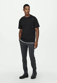 T-shirt preto de mangas curtas com decote branco, combinado com calças justas de padrão xadrez e botas de tornozelo pretas.